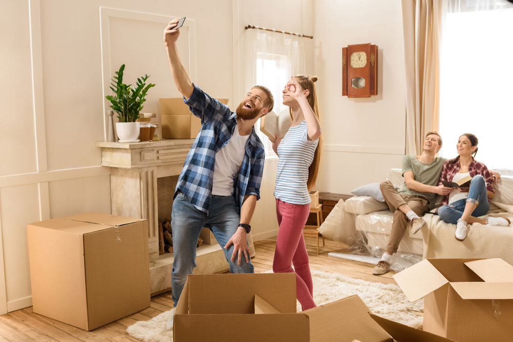 family moving into their new place. A girl and boy taking a selfie with a woman and man sitting on the sofa laughing