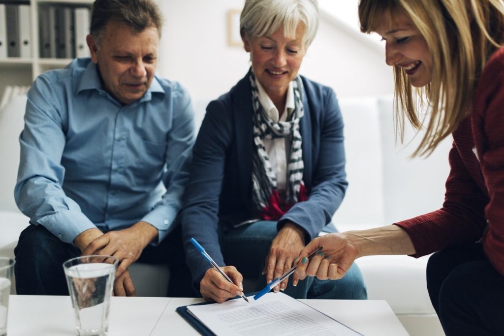 old couple signing a contract. A middle aged woman guiding them through it.